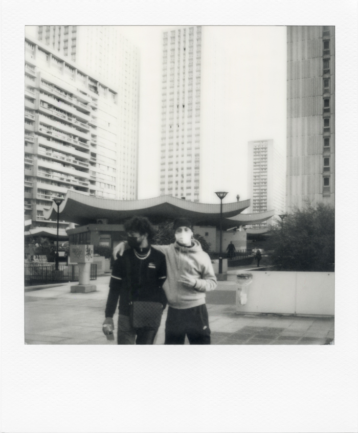 Black and white Polaroid of Paris. Two young people pose in front of the Olympiades district, Paris, 17 March 2021. Photo by Virginie Merle / Hans Lucas. 
Deux jeunes posent devant quartier des Olympiades, Paris, le 17 Mars 2021. Photo de Virginie Merle / Hans Lucas.
